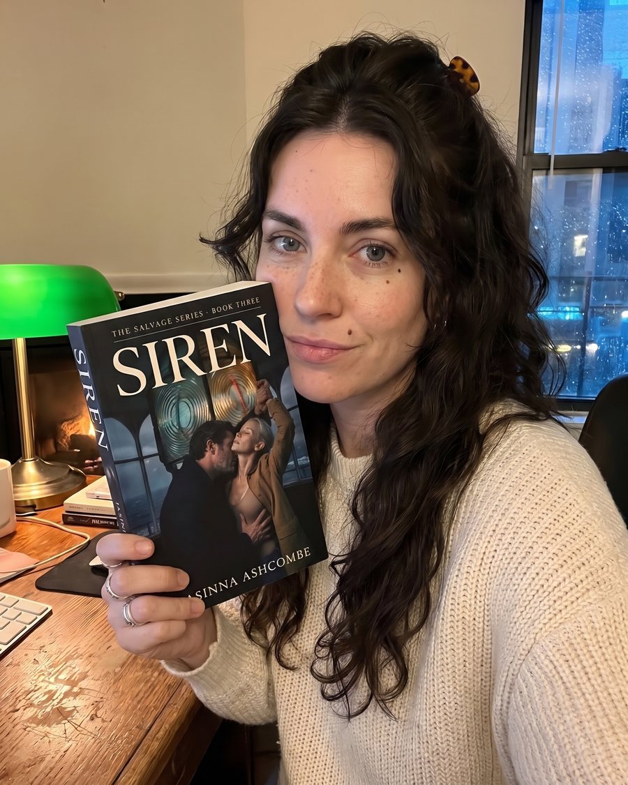 Jasinna Ashcombe at her desk at night, holding a copy of SIREN